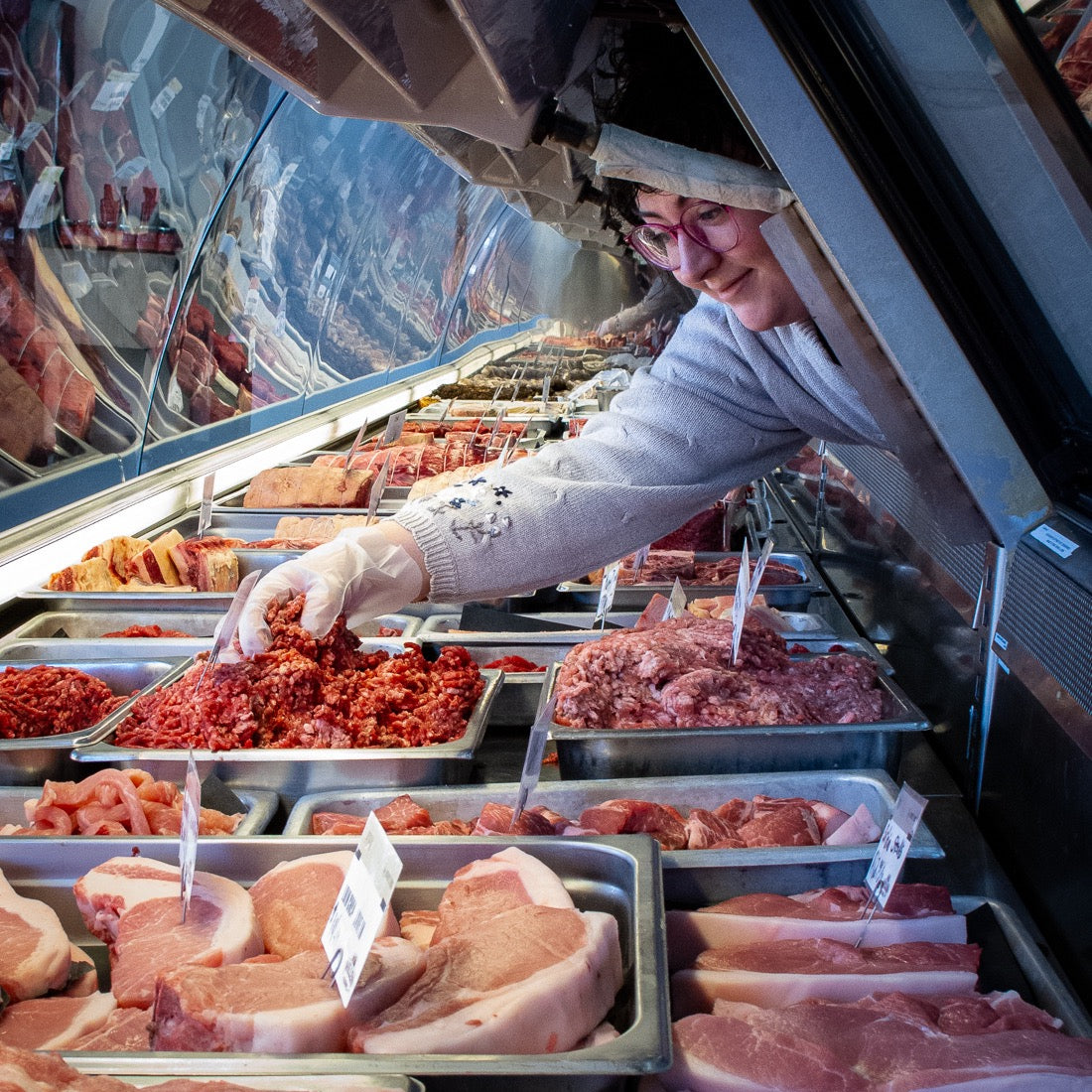 Inside of the Osprey's Roost meat counter with trays of different meats and an employee scooping up a handful of fresh ground beef